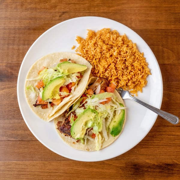 Two tacos with meat, lettuce, tomato, and avocado, served with a side of orange rice.