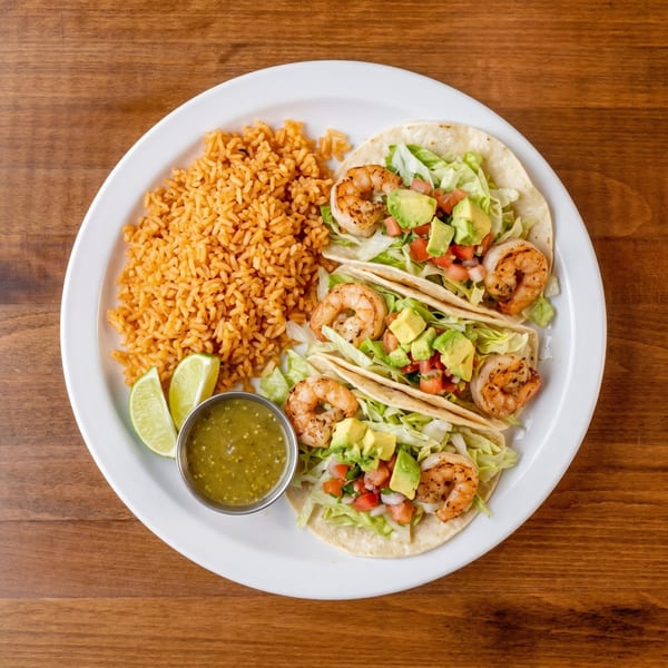 Three shrimp tacos with lettuce, avocado, and pico de gallo, served with rice, lime, and salsa verde.
